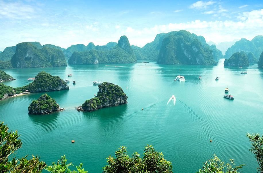 Limestone karst islands and tour boats in the emerald water of Ha Long Bay, Vietnam